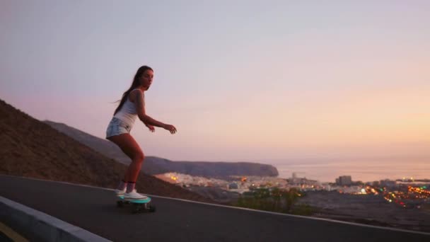 Krásná dívka jede na skateboardu na silnici proti západu slunce na obloze - Záběry, video