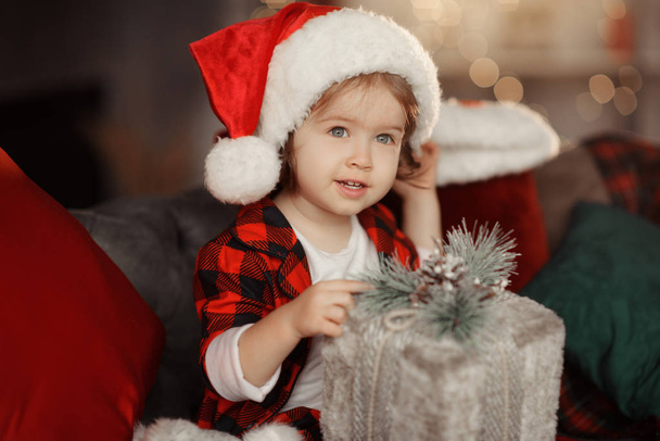 Noël mignon tout-petit fille dans le chapeau de Père Noël tenant une boîte-cadeau. Concept vacances en famille
. - Photo, image