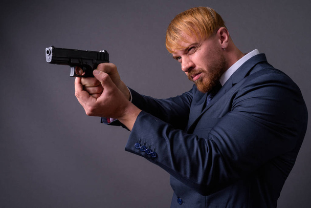 Bearded businessman with handgun against gray background - Foto, afbeelding