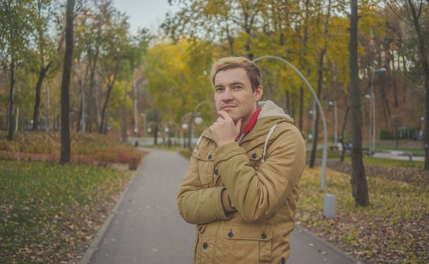 Young white guy, with yellow trees on background. Autumn season time. A student walks in the park. - Foto, afbeelding