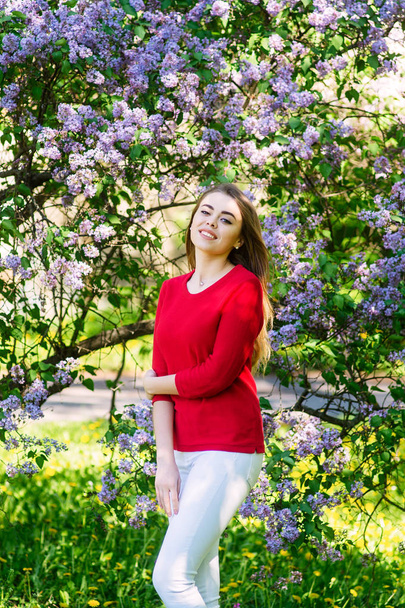 Young girl in a spring park. On the background of lilac flower. Smiling model. - Foto, Imagem