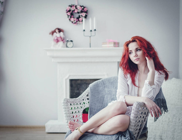 Girl with red hair in a light white shirt. classic interior filled with light - Foto, afbeelding