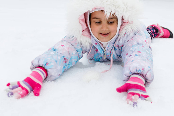 Маленька дівчинка в пухнастому пальто грає на сніжному дитячому майданчику
 - Фото, зображення