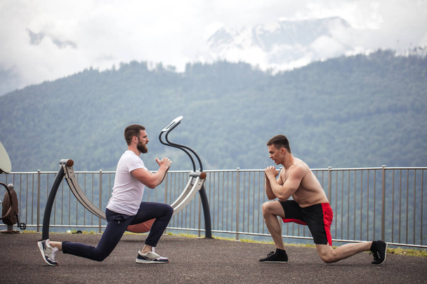 Side view of two caucasian sportsmen doing lungesin mountains. - 写真・画像