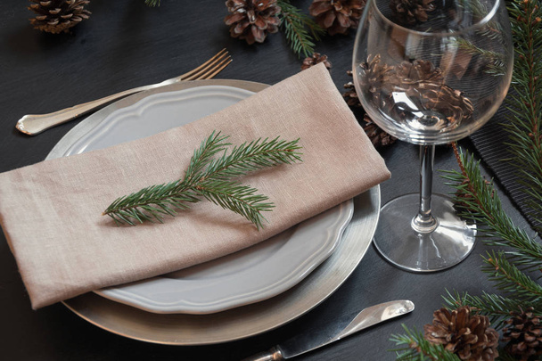 Christmas table setting with silverware and dark natural evergreen decor on black table. Close up. Holiday Centerpieces. - Foto, Bild