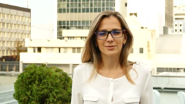 4K. Attractive woman in glasses looks at camera with smile, city business style. Steady shot - Footage, Video