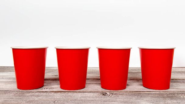 Four red empty take away disposable paper cups on wooden desk and white background. - 写真・画像