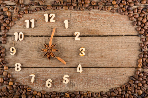 Dekorative Uhr mit Ziffern und Pfeilen aus Zimtstangen, die 4 Uhr zeigt, auf einem Holzgrund und einem Rahmen aus Kaffeebohnen. Küche, Werbung, Banner, Kopierraum, flach. - Foto, Bild