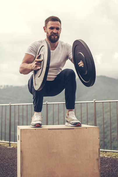 Strong male athlete doing box jumps with two plates outdoor on top of mountain. - Φωτογραφία, εικόνα