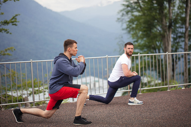 Side view of two caucasian sportsmen doing lunges in mountains. - 写真・画像