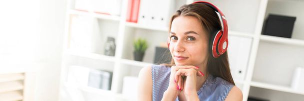 Beautiful young girl in the office sits at a table in red headphones. - Foto, afbeelding