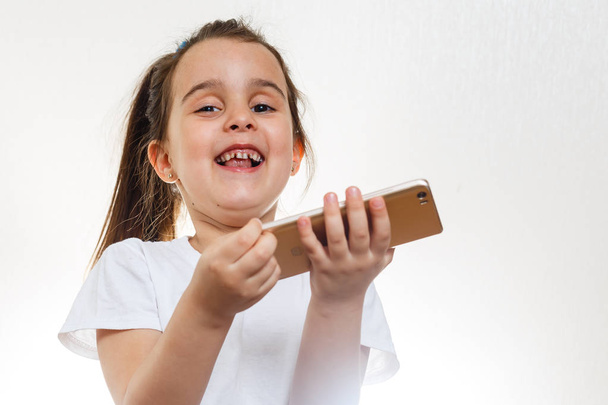 Brunette little girl holding smartphone on white background - Photo, Image