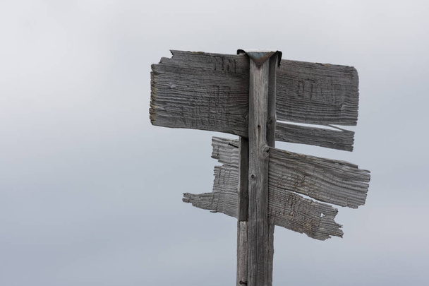 Oude en verweerde houten Wegwijzer in grijze kleur met gebroken onderdelen voor soepele wolken. - Foto, afbeelding
