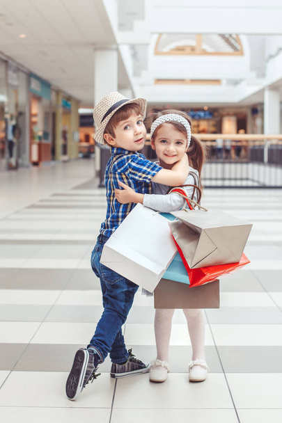 Portret grupy dwa cute adorable dzieci w wieku przedszkolnym zakupy. Kaukaski małej dziewczynki i chłopiec biegną w centrum handlowym. Dzieci trzymając torby na zakupy. Czarny piątek sprzedaż koncepcja.  - Zdjęcie, obraz