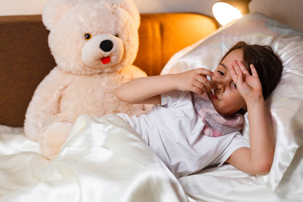 Sick little girl covered in blanket laying in bed  - Фото, зображення