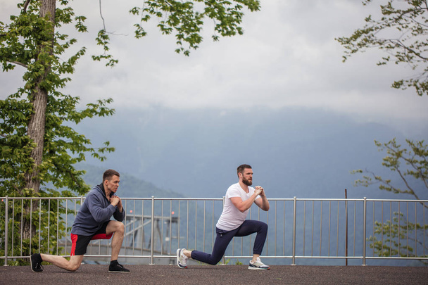 Side view of two caucasian sportsmen doing lunges in mountains. - Fotó, kép