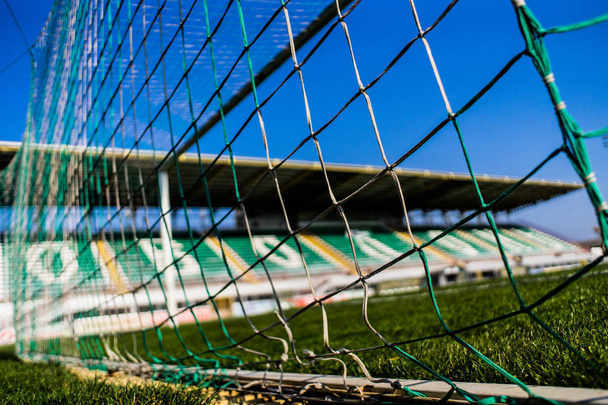 Voetbal goal net met kleine tribune op de achtergrond en de kleurrijke gras en de hemel - Foto, afbeelding