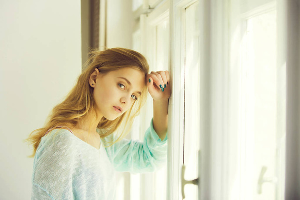Pretty girl with blue eyes standing at window - Photo, Image