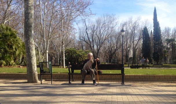 Madrid, Hiszpania - 24 stycznia 2018: Nieznany mężczyzna z psem spoczywa na ławce w parku w zabytkowym centrum Madrytu. Hiszpania - Zdjęcie, obraz