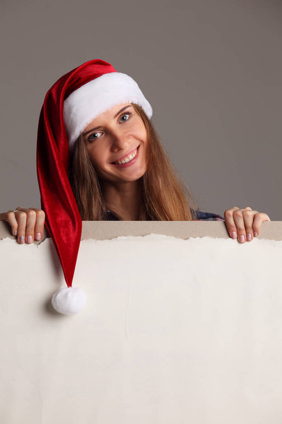 Santa girl holding blank vintage sign billboard. Christmas woman in Santa hat showing paper sign. - Fotografie, Obrázek