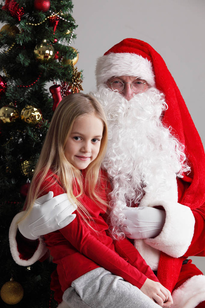 Portrait of smiling little girl sitting on santa claus knees - Zdjęcie, obraz