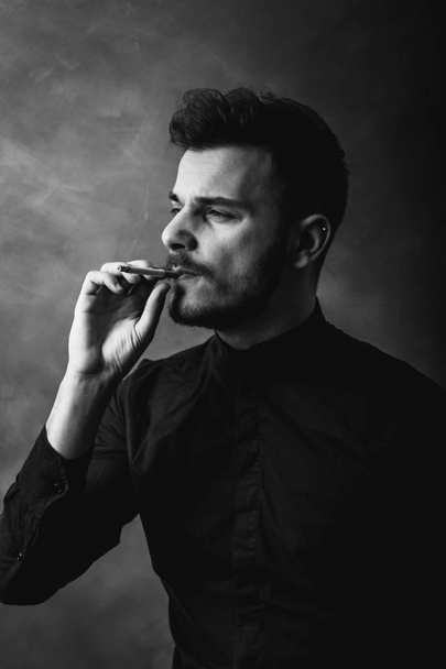 Portrait of young man smoking cigarette in art studio - Zdjęcie, obraz