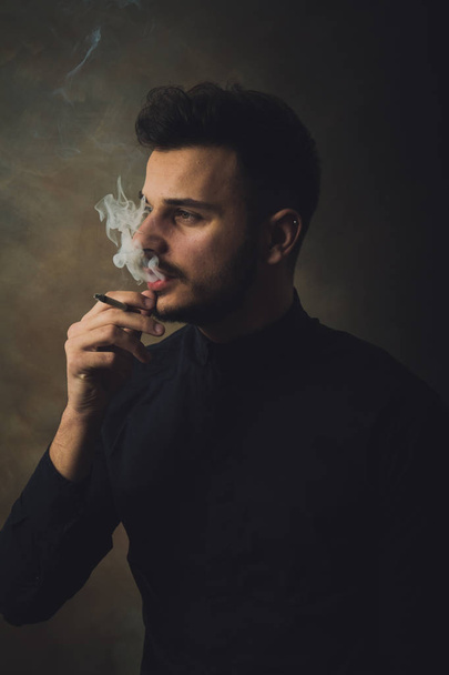 Portrait of young man smoking cigarette in art studio - 写真・画像