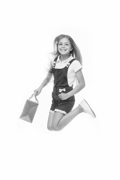 Happy child jump with shopping bag isolated on white. Little shopaholic smile with paper bag in motion. Girl shopper celebrate purchase. Shopping and sale. Black Friday - Фото, зображення