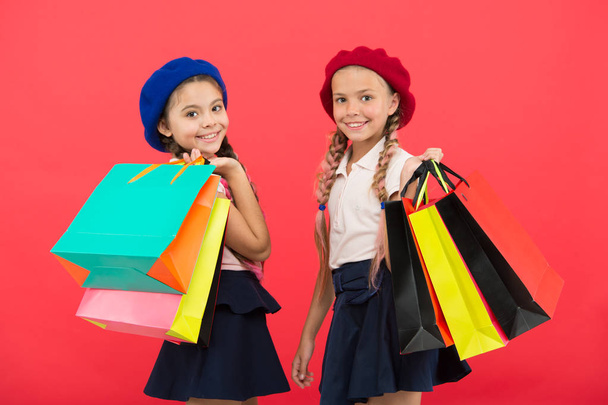 Shopping become fun with best friends. Kids cute schoolgirls hold bunch shopping bags. Children satisfied by shopping red background. Obsessed with shopping and clothing malls. Shopaholic concept - 写真・画像