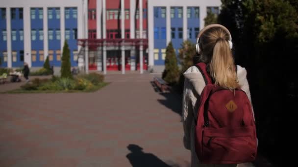 Suloinen koulutyttö kävelee kohti koulurakennusta
 - Materiaali, video