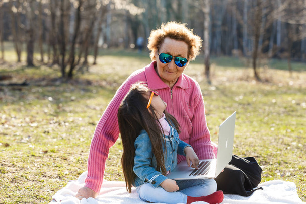 Meisje met grootmoeder met laptop in voorjaar park - Foto, afbeelding