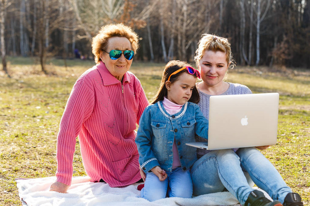 Три покоління сім'ї використовують ноутбук у парку
 - Фото, зображення