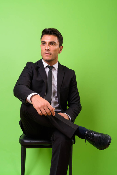 Young handsome Hispanic businessman against green background - Photo, image