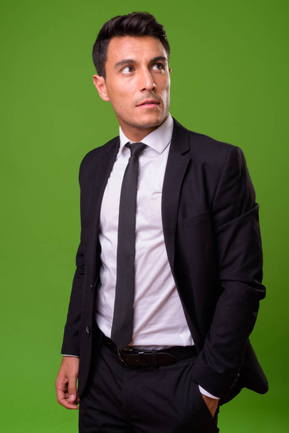 Young handsome Hispanic businessman against green background - 写真・画像