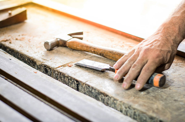 Primer plano de las manos de un carpintero que trabaja con un cincel y un martillo en un banco de trabajo de madera
 - Foto, Imagen