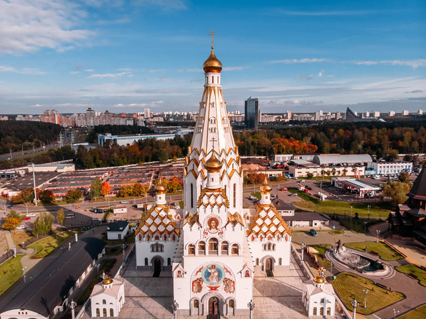 Vista superior da frente majestoso templo alto com cúpulas douradas, telhas laranja no fundo paisagem urbana e azul céu de outono ensolarado. República de Minsk da Bielorrússia. Drone aéreo
 - Foto, Imagem