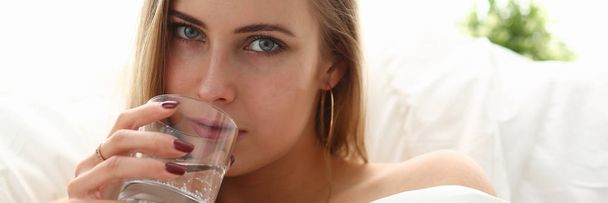 blond woman hold glass of water in arm early morning stay in bed - Photo, Image
