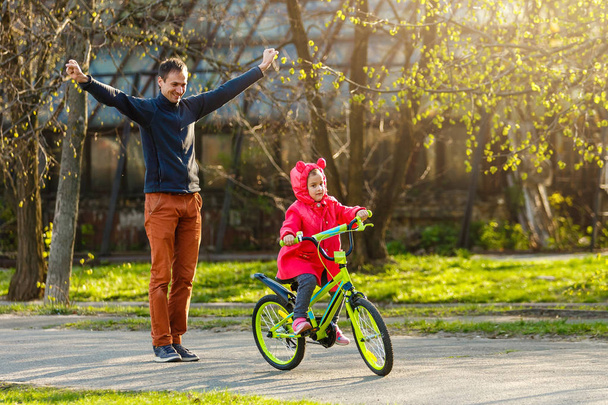 Mała dziewczynka jeździ rowerem i szczęśliwym ojcem po córce w zielonym parku - Zdjęcie, obraz