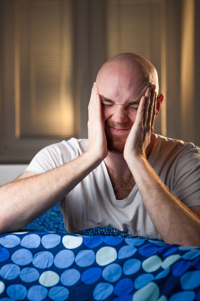Молодой человек в постели с головной болью, депрессией и зевотой от похмелья
 - Фото, изображение