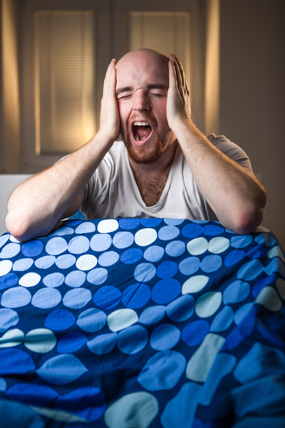 Молодой человек в постели с головной болью, депрессией и зевотой от похмелья
 - Фото, изображение