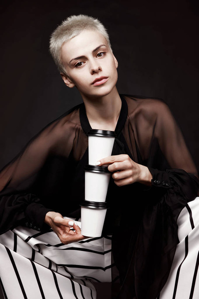 Emotional young girl with short hair and paper coffee cups on black background. coffee to go. Advertising. - 写真・画像