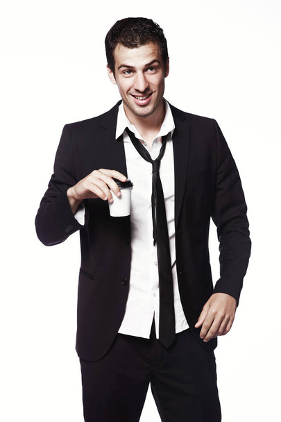 Un joven con un traje negro y una taza de café sobre fondo blanco. Publicidad, creatividad. Café para llevar
. - Foto, Imagen