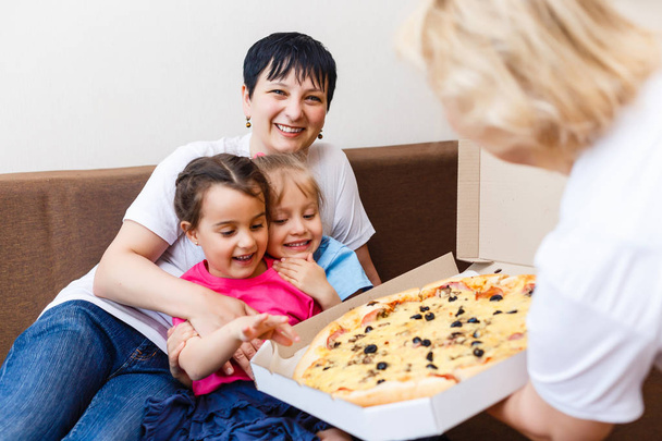 Äiti ja isoäiti, joilla on lapsia, jotka syövät suurta pizzaa kotona
 - Valokuva, kuva