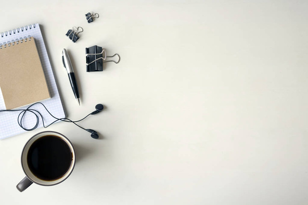 weißer Holztisch mit Kopfhörer, Stift, Notizbuch, Dokumentenklemmen und einer Tasse Kaffee. Arbeitsbereich von oben mit Kopierraum. - Foto, Bild