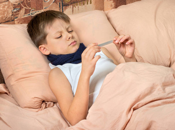 Niño enfermo en la cama viendo la temperatura en el termómetro
 - Foto, Imagen