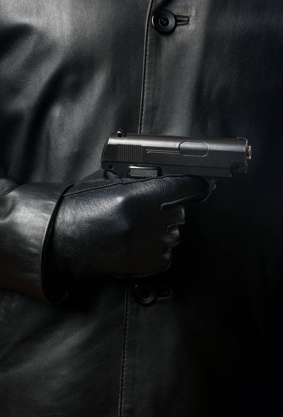 Bandit σε ένα μαύρο σακάκι με γάντια με ένα πυροβόλο όπλο γκρο πλαν - Φωτογραφία, εικόνα