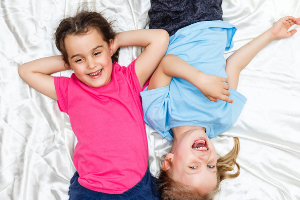 Вид зверху на щасливих маленьких дівчат, що лежать на білих простирадлах
 - Фото, зображення