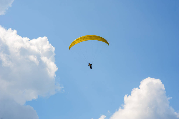 Paralotnia leci w błękitne niebo chmury na tle. Paralotniarstwo w niebo na słoneczny dzień. - Zdjęcie, obraz