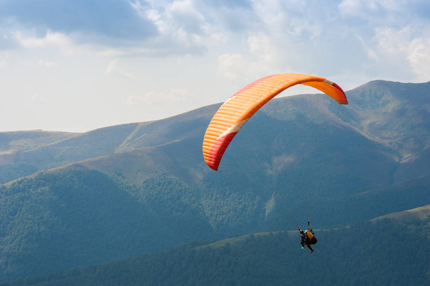 Laskuvarjohyppääjä lentää vuoristolaakson yli aurinkoisena kesäpäivänä. Varjoliito Karpaateilla kesällä
. - Valokuva, kuva