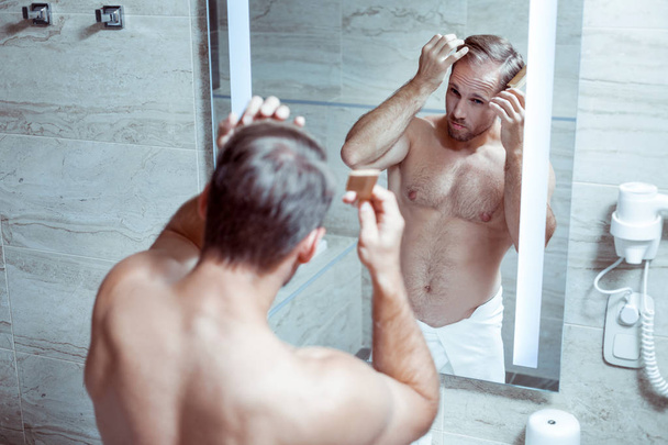 Athletic handsome man combing his hair standing in the bathroom - Foto, Imagem